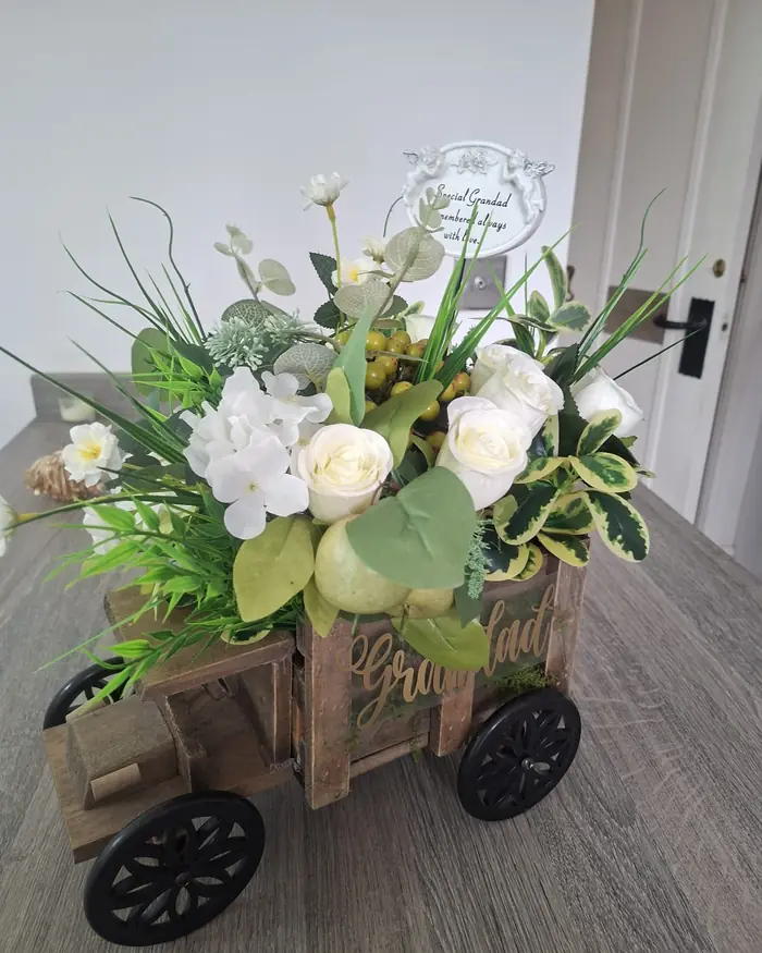 Cream and white roses with eucalyptus in a small wooden cart planter, indoors beside a door.