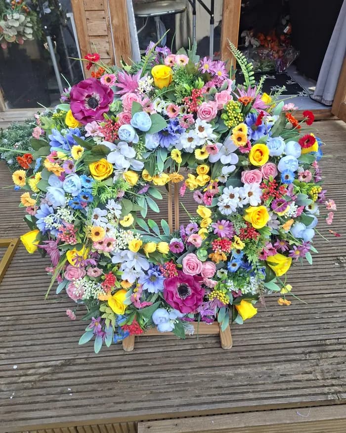 A bright spring wreath of yellow, pink, blue and lilac blooms, propped on decking.