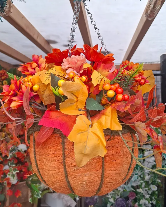 An orange pumpkin-shaped hanging basket trailing maple leaves and berries, hung in a summerhouse.