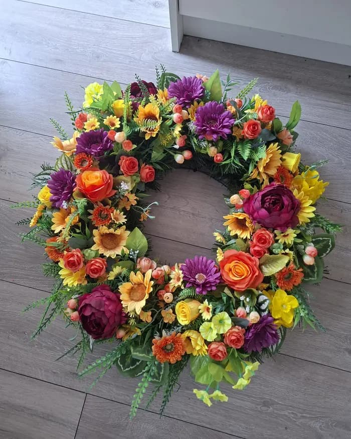 A wreath of yellow, orange and deep purple blooms on grey decking.