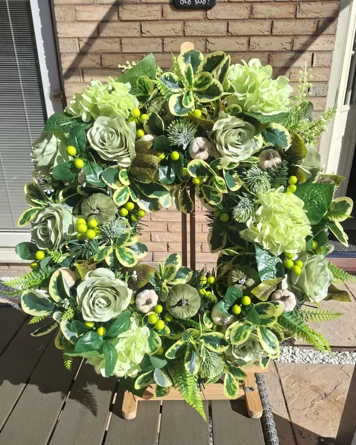 A green and white wreath of roses, berries and foliage on an easel against brickwork.