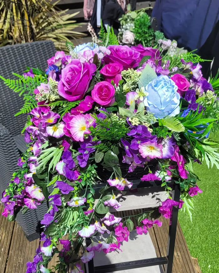 A purple, magenta and blue spray with ferns and trailing blooms, on a black garden chair.