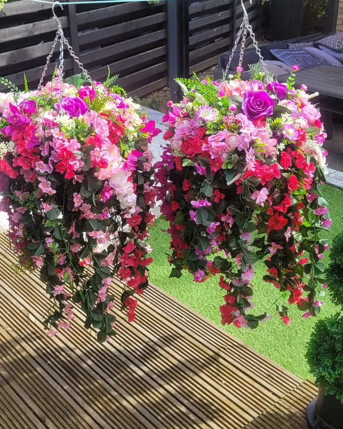 Two matching pink cascading hanging baskets hanging above a lawn.
