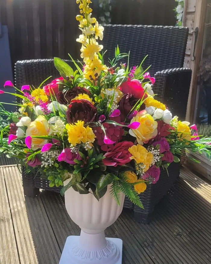 A bright mixed arrangement of roses and tulips in a white urn, on decking.