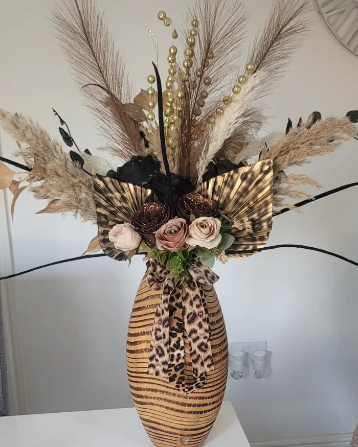 Pampas grass and dried stems arranged in a tall leopard-print vase, indoors.