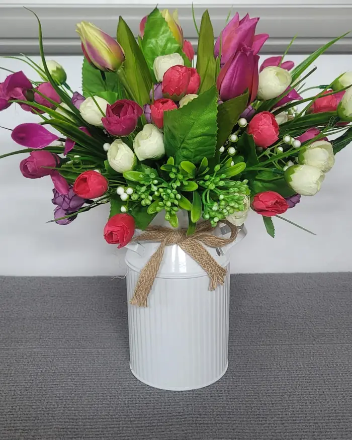Pink and white tulips with green foliage in a white ribbed pot, tied with hessian.