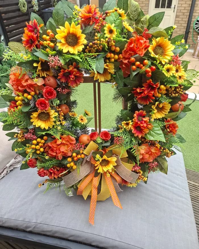 An orange sunflower and berry autumn wreath with a ribbon, displayed on an easel.