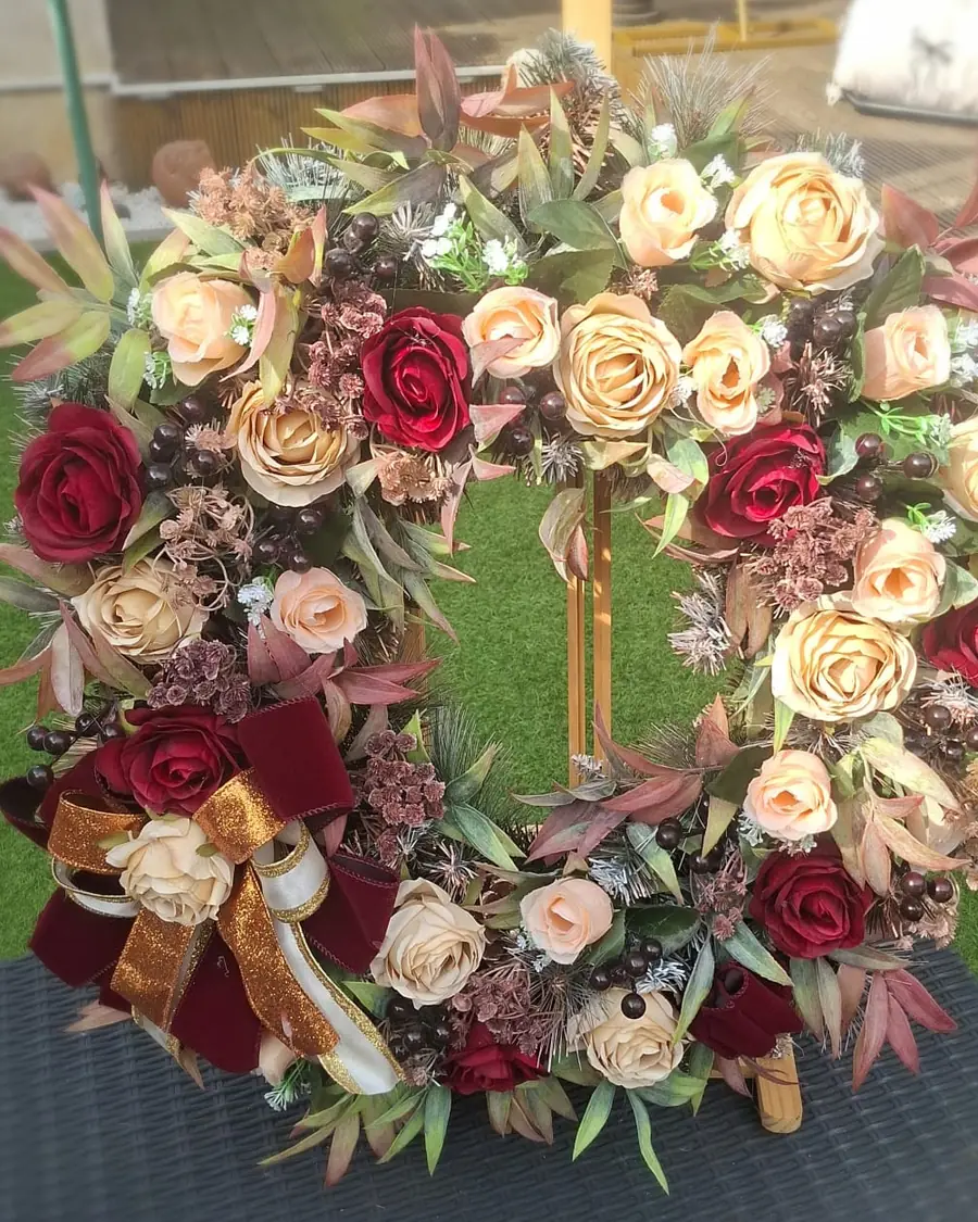 A 60cm autumn wreath of burgundy and champagne roses with dark berries and a burgundy velvet and gold ribbon bow.