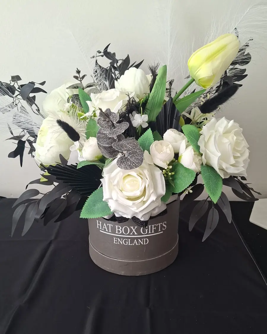 A grey hat box of white roses and tulips with black palm spears and white pampas.