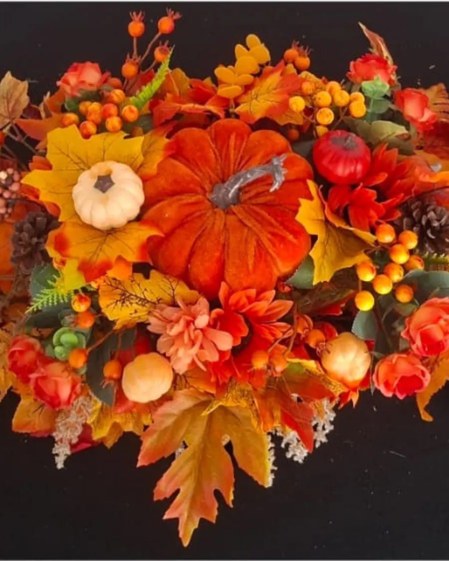A long, low autumn table centrepiece of orange pumpkins, maple leaves, berries and ferns, arranged on black cloth.