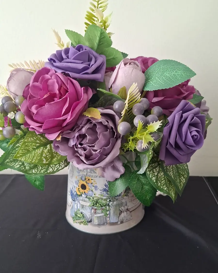 A small painted tin jug filled with magenta and lilac roses and peonies with grey berries.