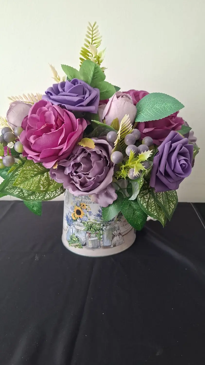 A small painted tin jug filled with magenta and lilac roses and peonies with grey berries.