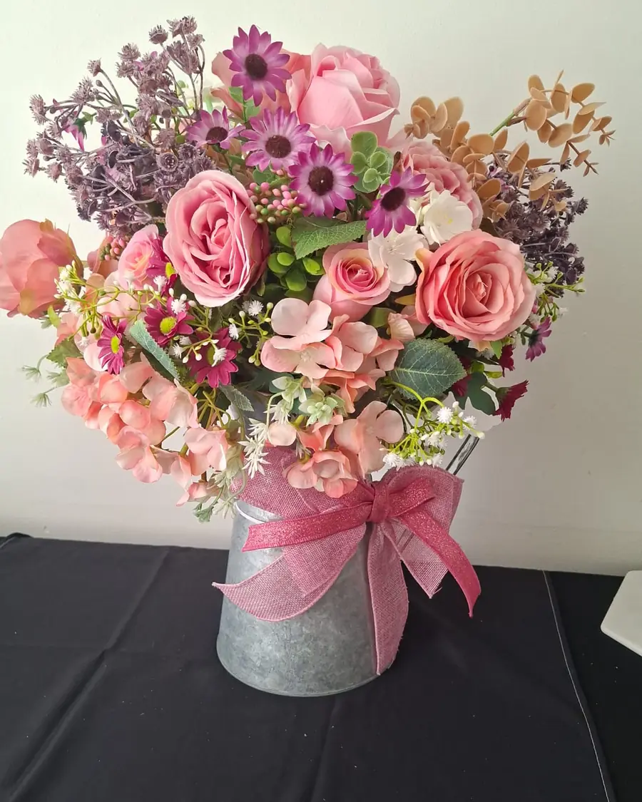 A galvanised tin filled with pink roses, sweet peas, lilac and purple daisies, tied with a pink hessian bow.