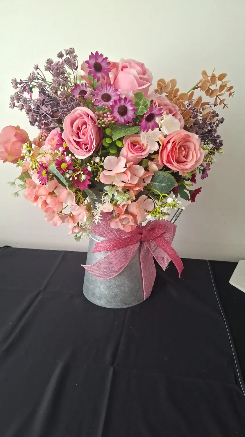 A galvanised tin filled with pink roses, sweet peas, lilac and purple daisies, tied with a pink hessian bow.