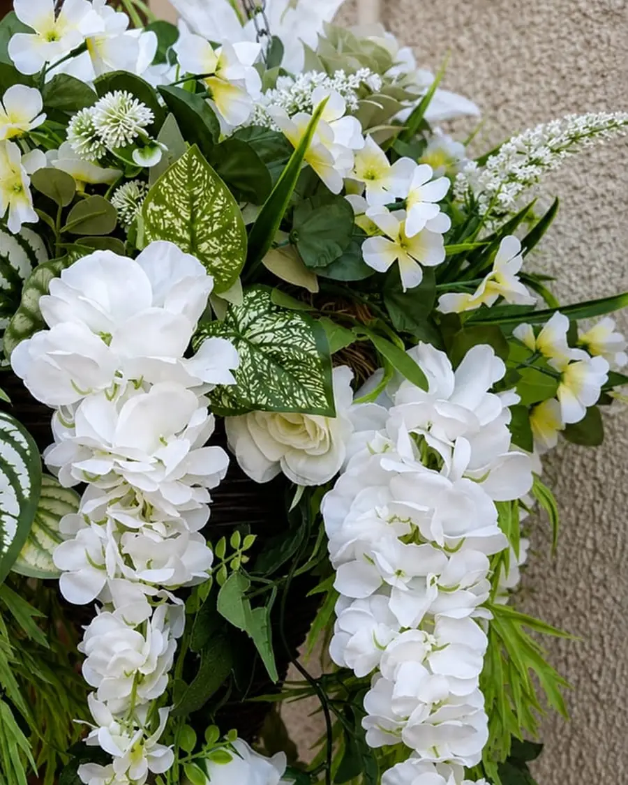 A wicker hanging basket of white hydrangeas and trailing wisteria beside a brick porch.