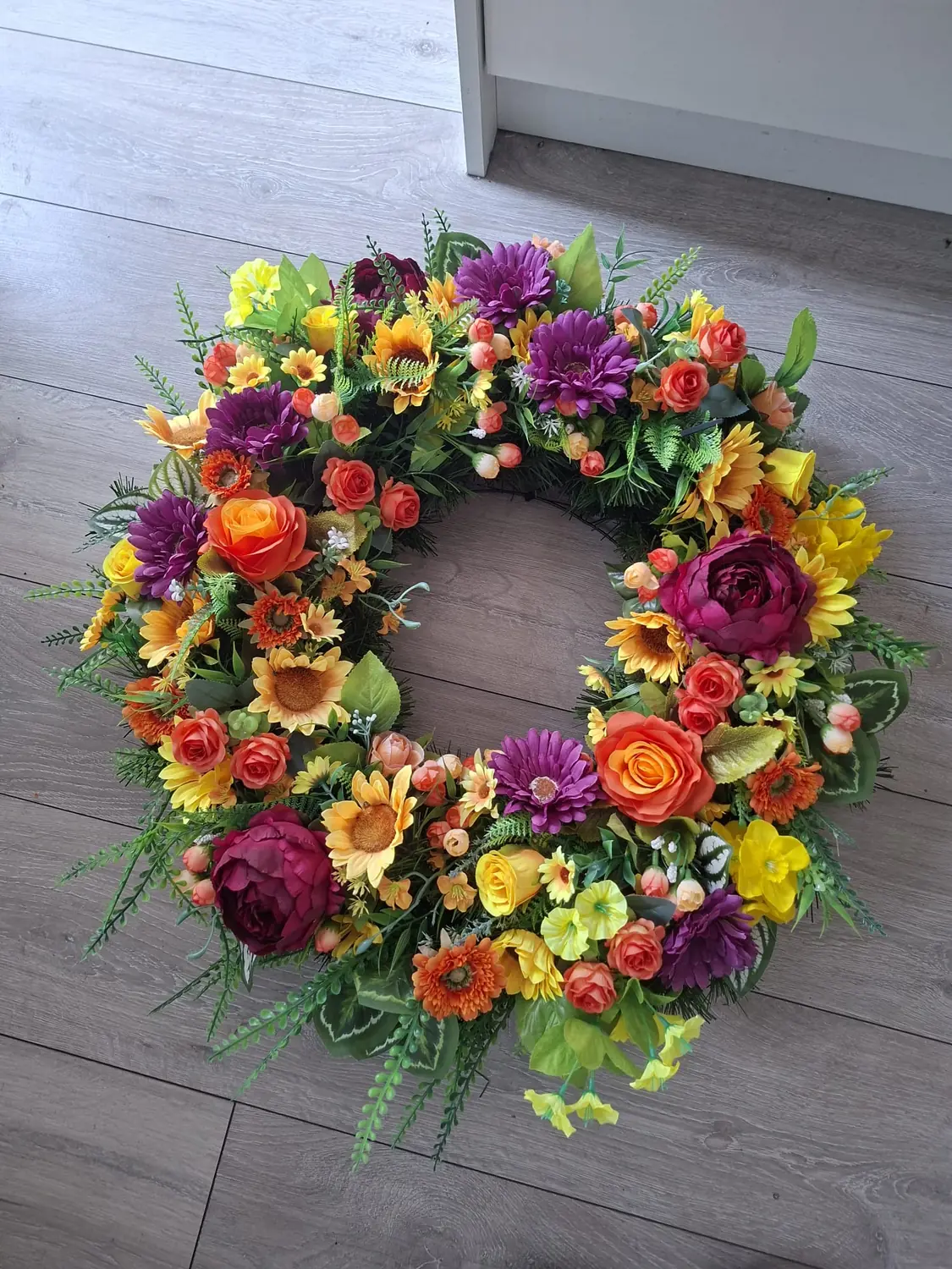 A wreath of yellow, orange and deep purple blooms on grey decking.